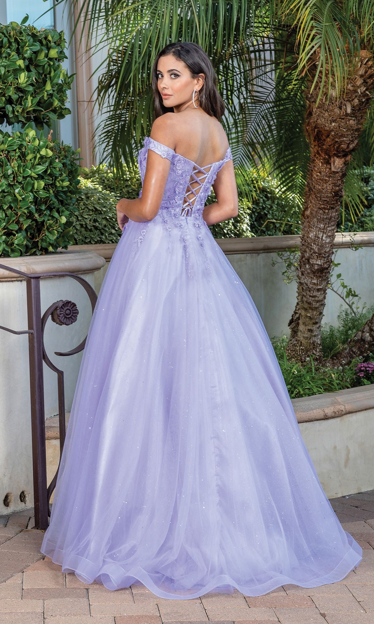 A woman stands outdoors near lush greenery and a palm tree, facing away in an Off-Shoulder Prom Ball Gown with Corset Back.